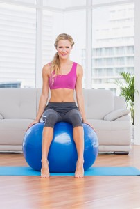 Toned blonde sitting on exercise ball smiling at camera